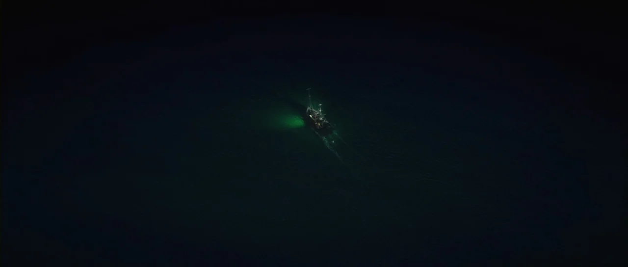 Grabbers (2012) movie still: establishing — A dark, expansive body of water is illuminated by a small vessel. The boat emits a green glow while…
