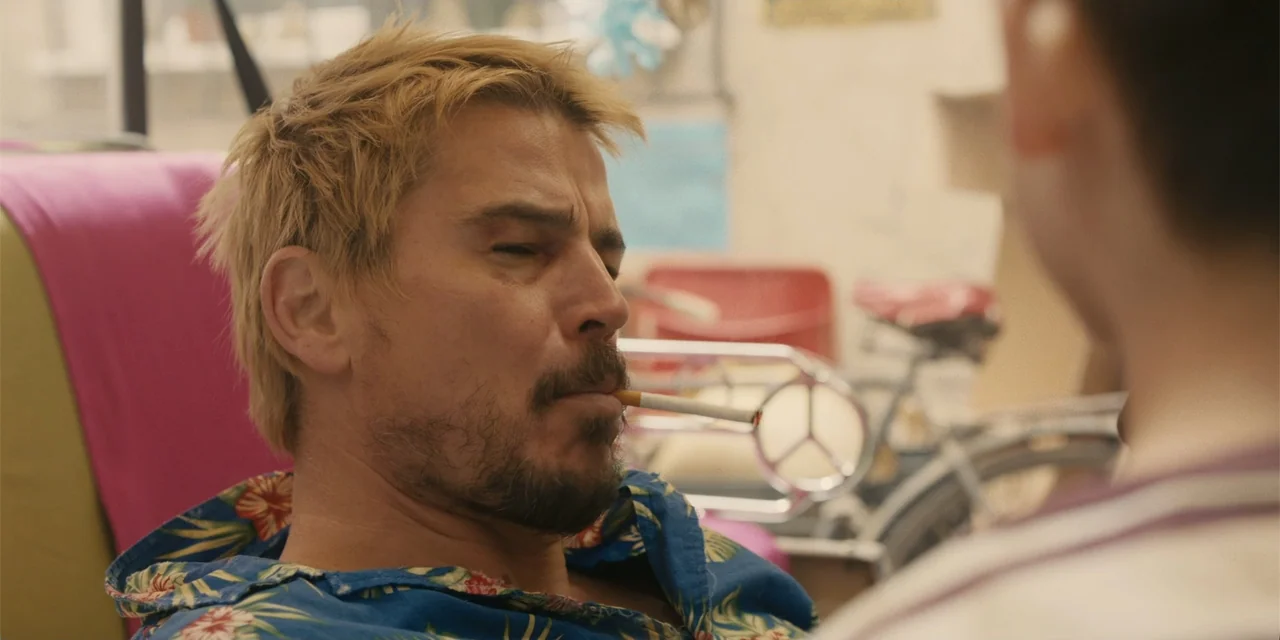 Fight or Flight (2025) movie still: closeup — A cluttered interior space serves as the backdrop for a conversation between two people. A man with…