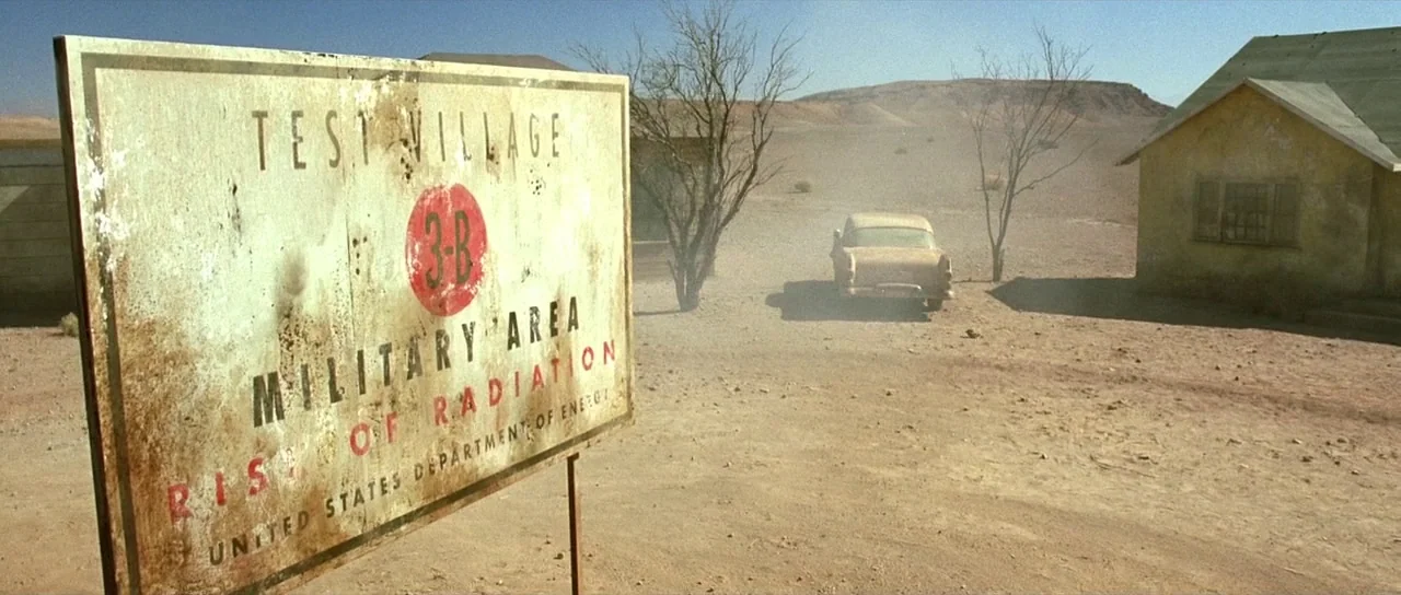 The Hills Have Eyes (2006) movie still: wide — A desolate desert test village features a prominent weathered warning sign in the foreground. A…