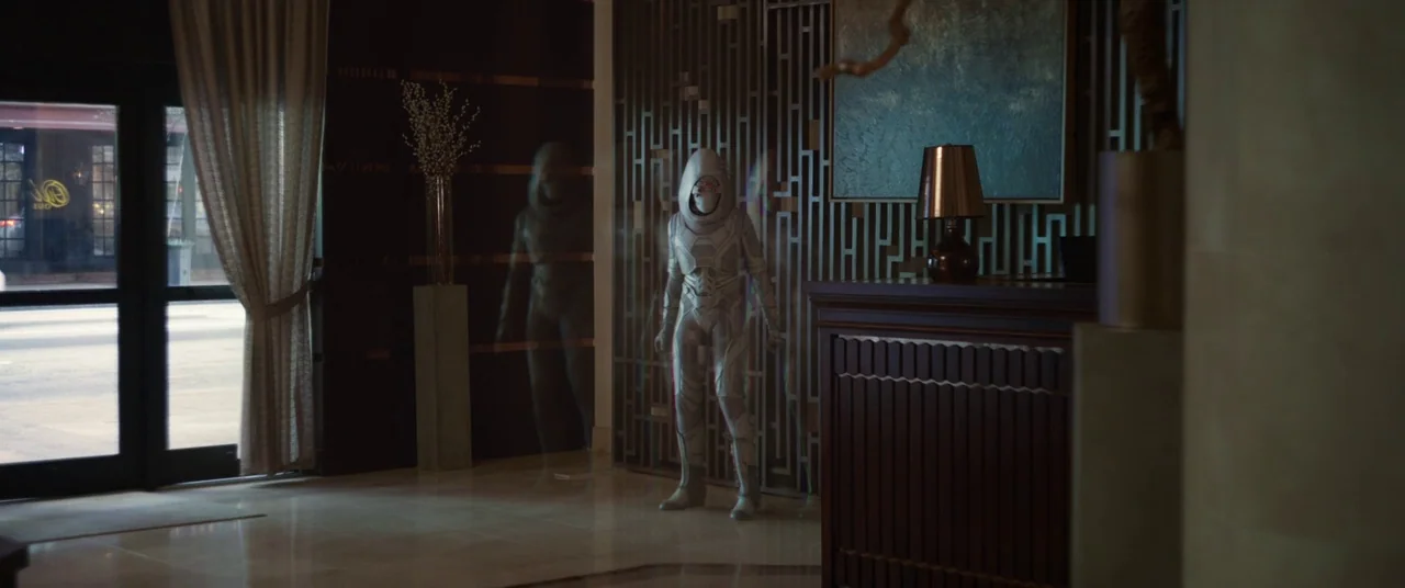 Ant-Man and the Wasp (2018) movie still: fullbody — A quiet lobby features dark wooden geometric panels and a large framed artwork. A person in a…