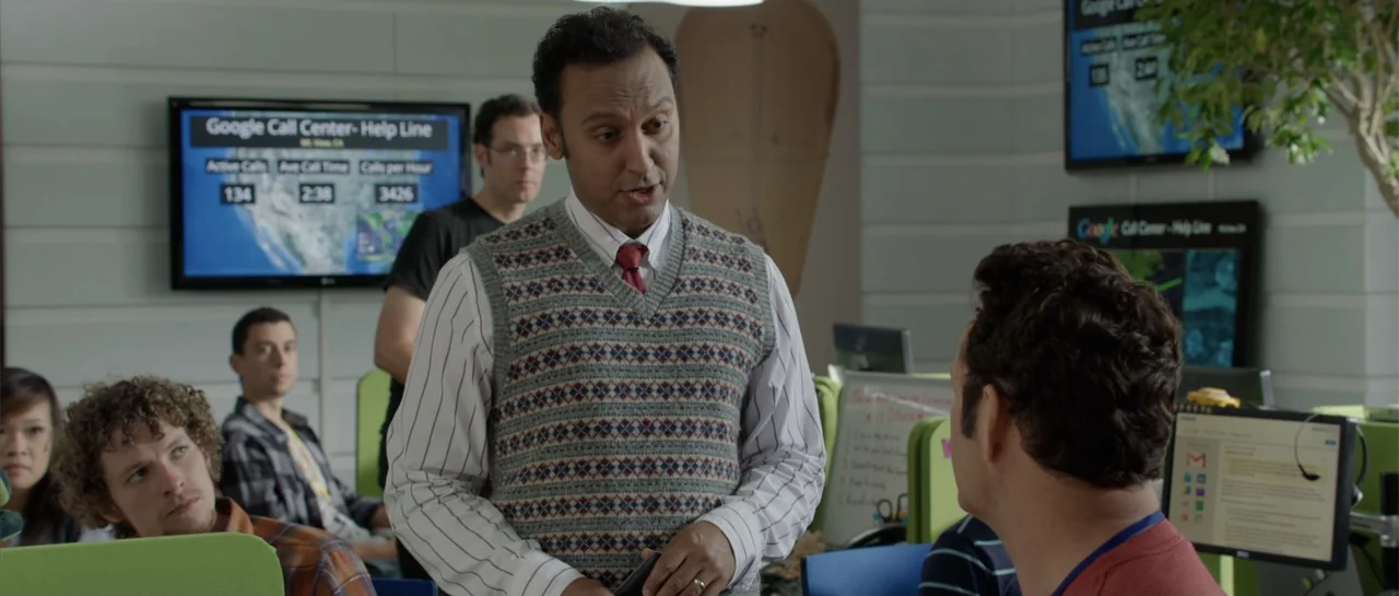 The Internship (2013) movie still: medium — A modern corporate office workspace features computer monitors and green plastic desk dividers. A man…