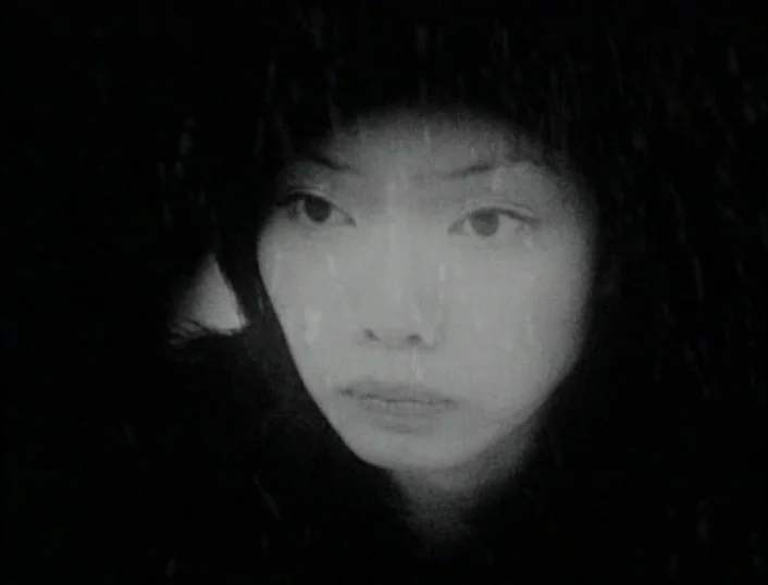 Cowards Bend The Knee (2003) movie still: closeup — A woman stands outdoors in a dark environment with light snow falling heavily. The camera…