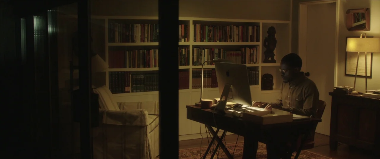 Da Sweet Blood of Jesus (2014) movie still: wide — A study with floor-to-ceiling bookshelves and a large wooden writing desk. A man works alone on a…
