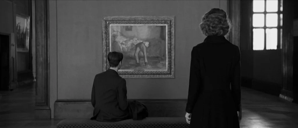 Frantz (2016) movie still: fullbody — A quiet room within an art museum features a large painting on a wall. A man sits on a bench while a woman…