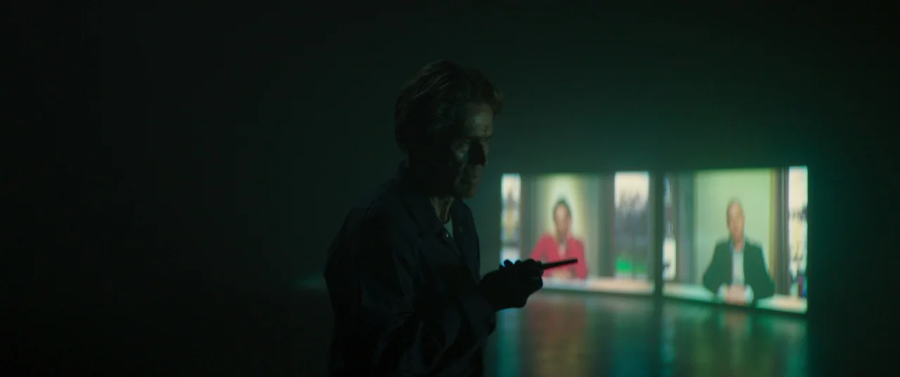 Inside (2023) (2023) movie still: medium — A man stands in a dark, empty space illuminated only by two distant glowing screens. He holds a small,…