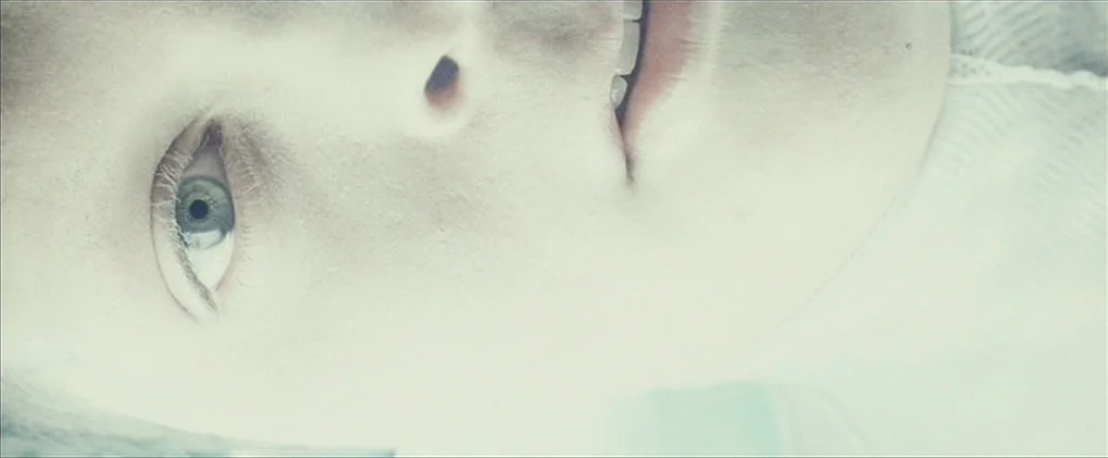Minority Report movie still: closeup — A close-up view shows a person's face against a stark white background. The subject lies horizontally in the…
