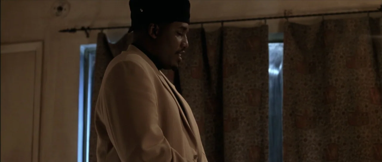 Gang Related (1997) movie still: medium — An interior space features a dark window covered by patterned, heavy drapes. A man in a tan overcoat and…