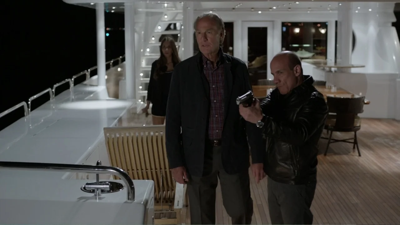 Get Hard (2015) movie still: fullbody — A luxury yacht deck at night features polished white surfaces and wooden floor slats. An armed man stands…