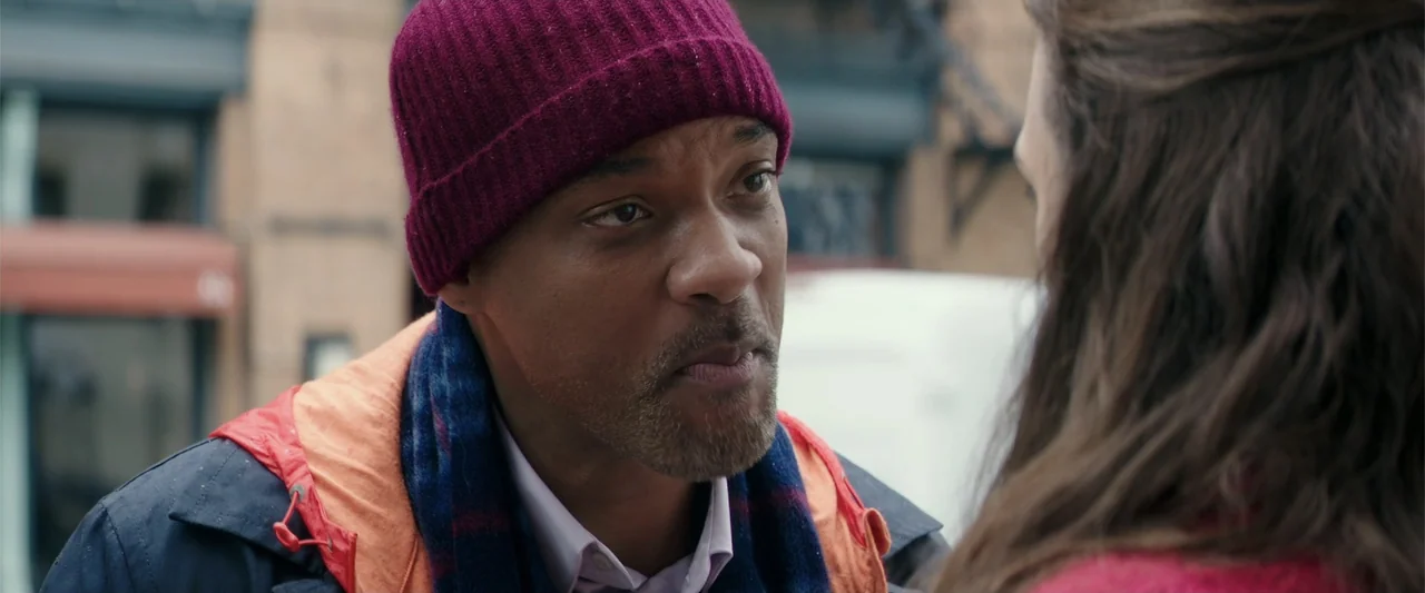 Collateral Beauty (2016) movie still: closeup — A busy urban street provides the backdrop for a close interaction between two people. A man wearing…