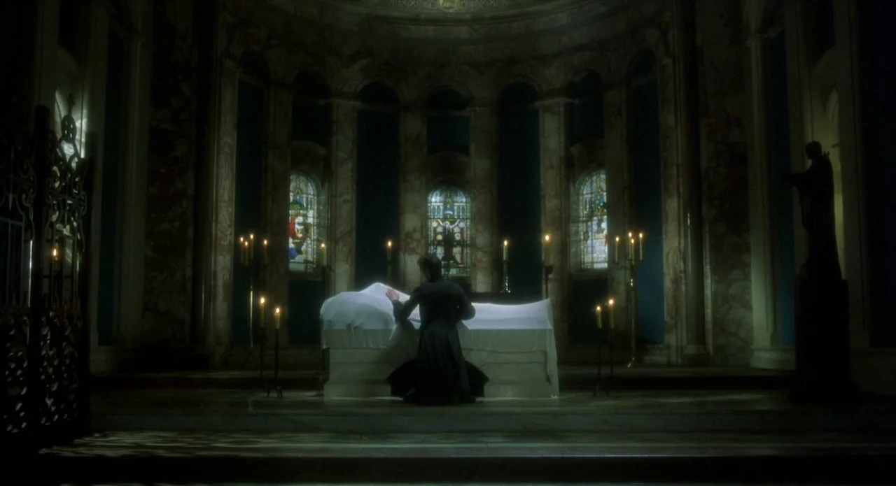 Quills (2000) movie still: wide — An interior of a cathedral nave features marble walls and tall arched windows. A person kneels in front of a…
