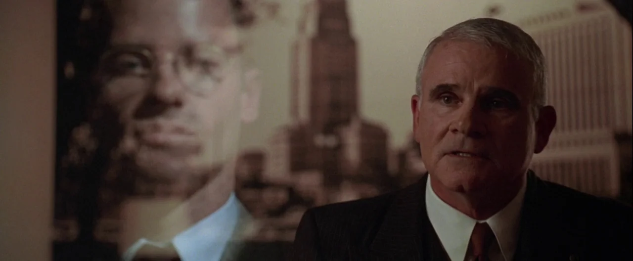 L.A. Confidential (1997) movie still: medium — An office interior features a wall displaying a large, faded black-and-white architectural portrait…