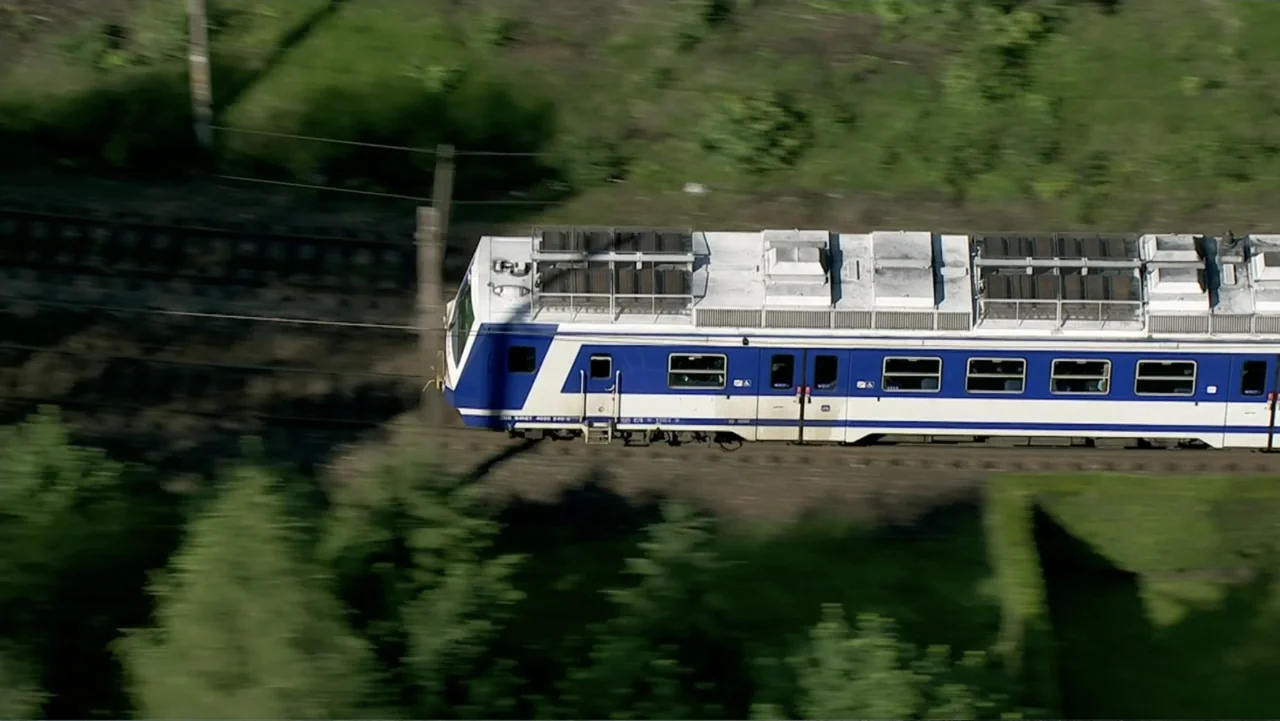 The Alps from Above: Symphony of Summits (2014) movie still: wide — A passenger train moves along tracks passing through dense green trees and…