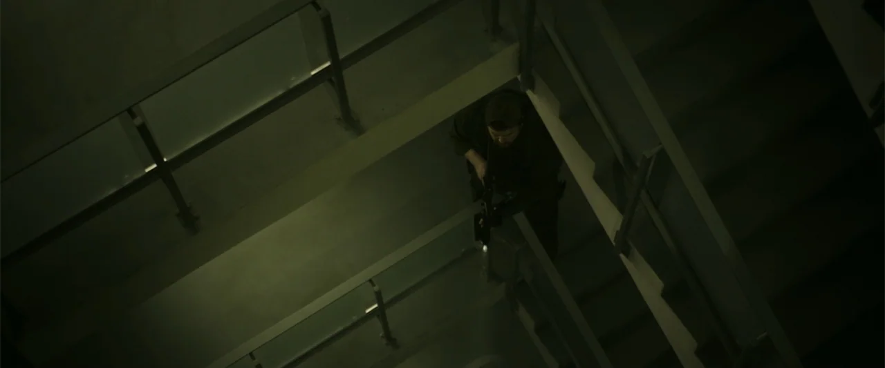 The Tomorrow War (2021) movie still: wide — A modern concrete stairwell with glass railings descends into darkness from a high angle. A man dressed…