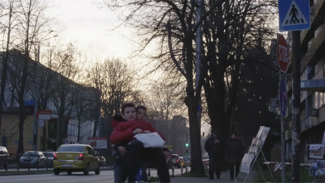 Finding the Way Home (1991) movie still: medium — A city street at dusk features bare trees and traffic in the background. Two young boys in red…