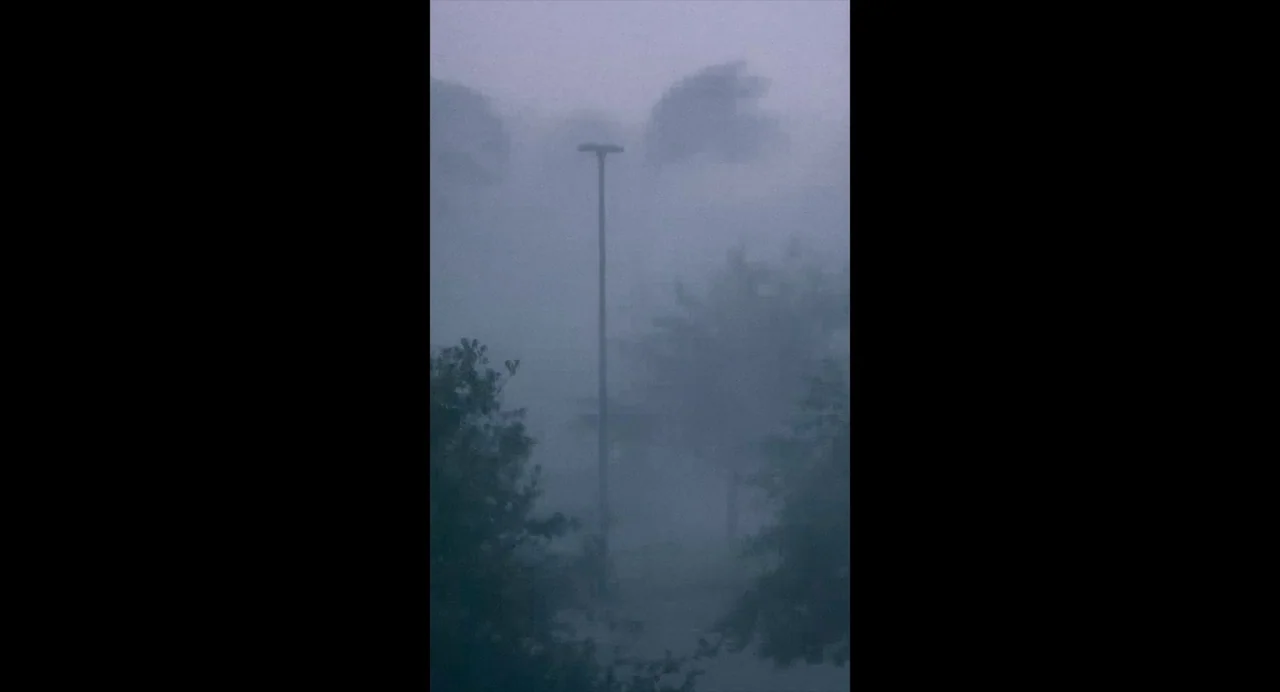 White River (2023) movie still: establishing — A storm rages in an outdoor space with heavy rain and wind. A tall light pole stands centrally amidst…