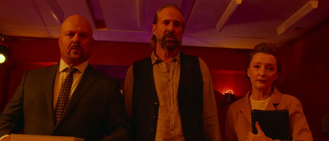 Rupture (2016) movie still: medium — A dimly lit room filled with deep red light and overhead fluorescent panel fixtures. Three individuals stand…