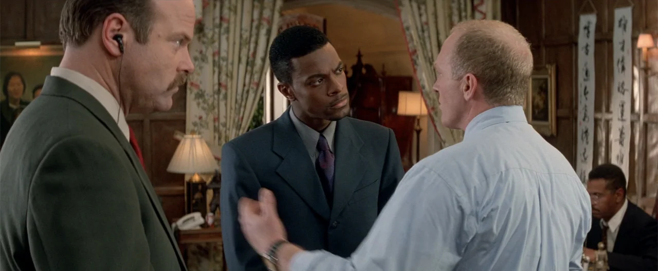 Rush Hour (1998) movie still: medium — A paneled study features wood-lined walls and floral curtains hanging by a window. Three men stand in…