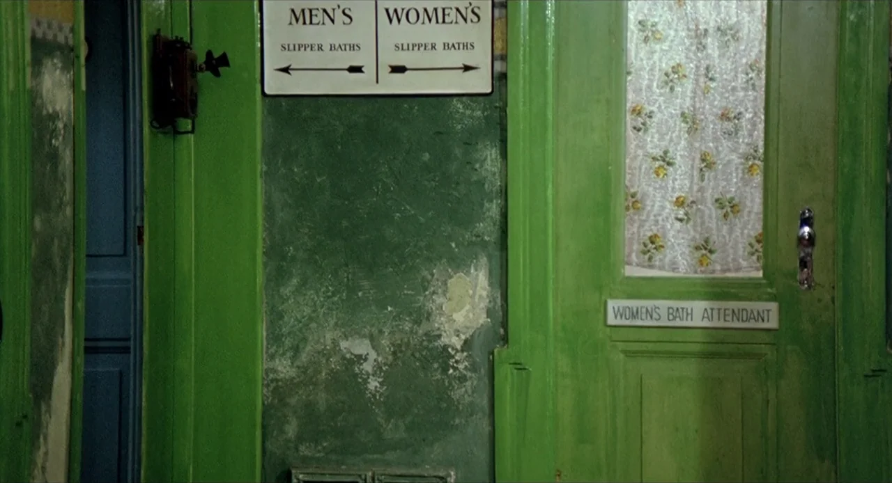 Deep End (1970) movie still: medium — An interior wall of a public bathhouse features bright green paint and peeling plaster. Wooden doors with…
