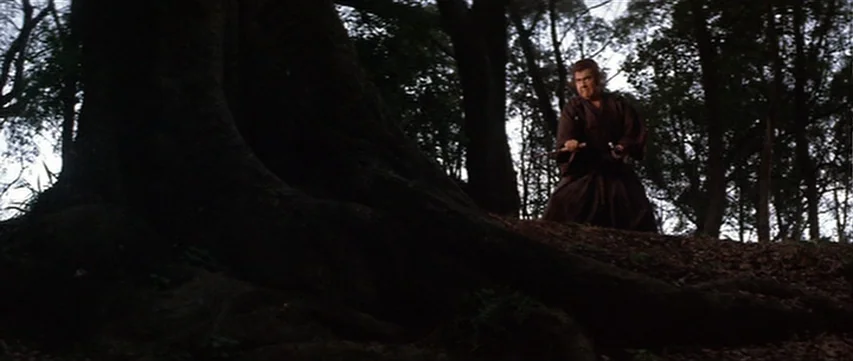 Lone Wolf: Baby Cart at the River Styx (1972) movie still: wide — A dense, dark woodland environment with large tree roots dominating the foreground…