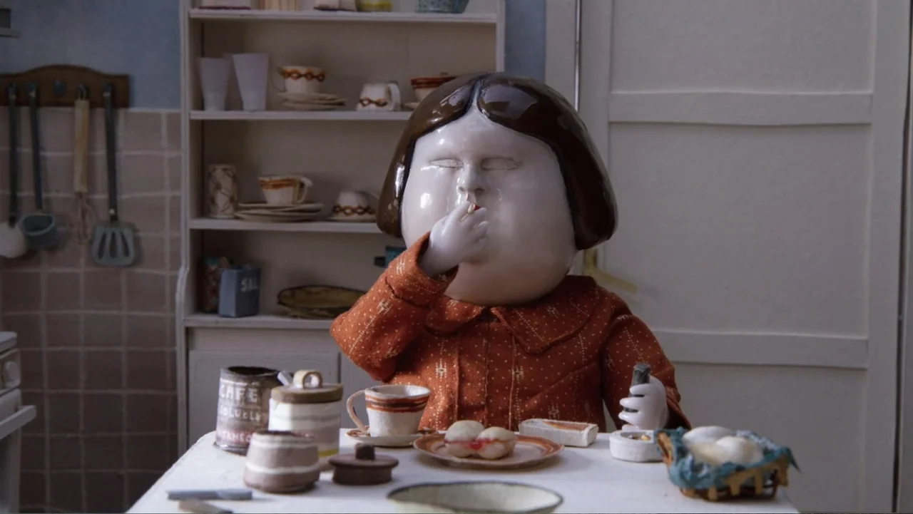 Bestia (2017) movie still: medium — A ceramic doll sits at a small table inside a rustic room. The character holds a tiny item to its mouth while…