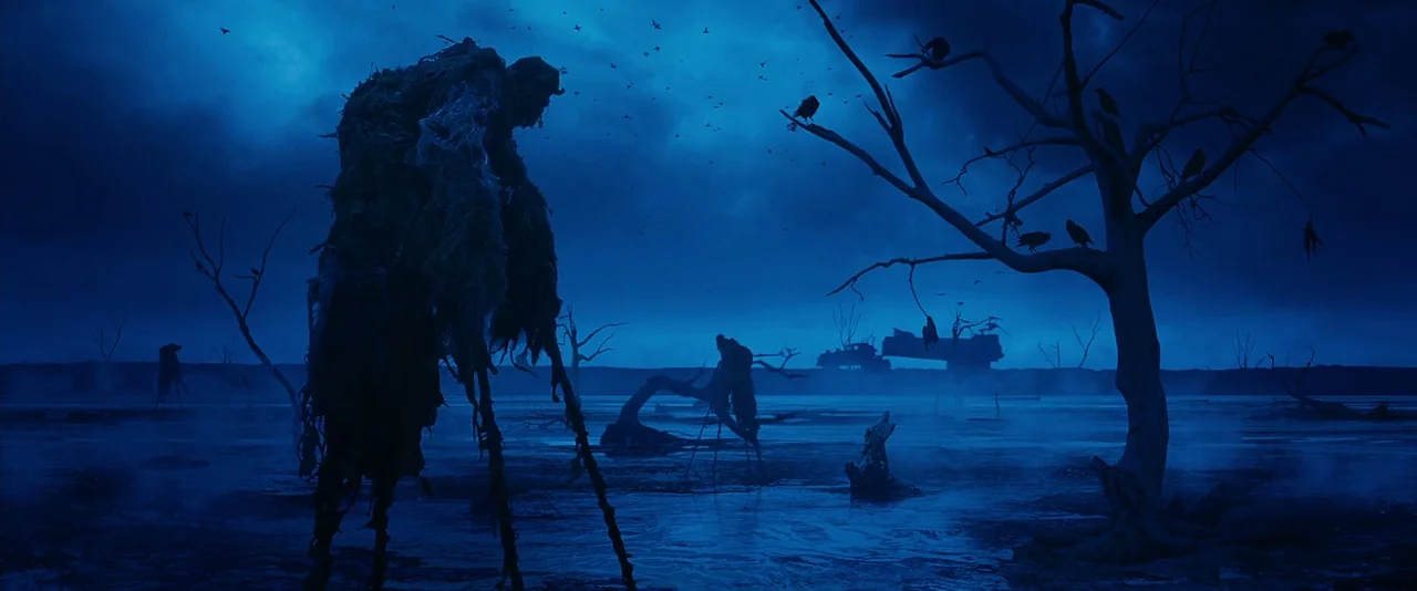 Mad Max: Fury Road (2015) movie still: wide — A dark, misty wetland at night features sparse, bare trees and shadowy, thin structures. Numerous…