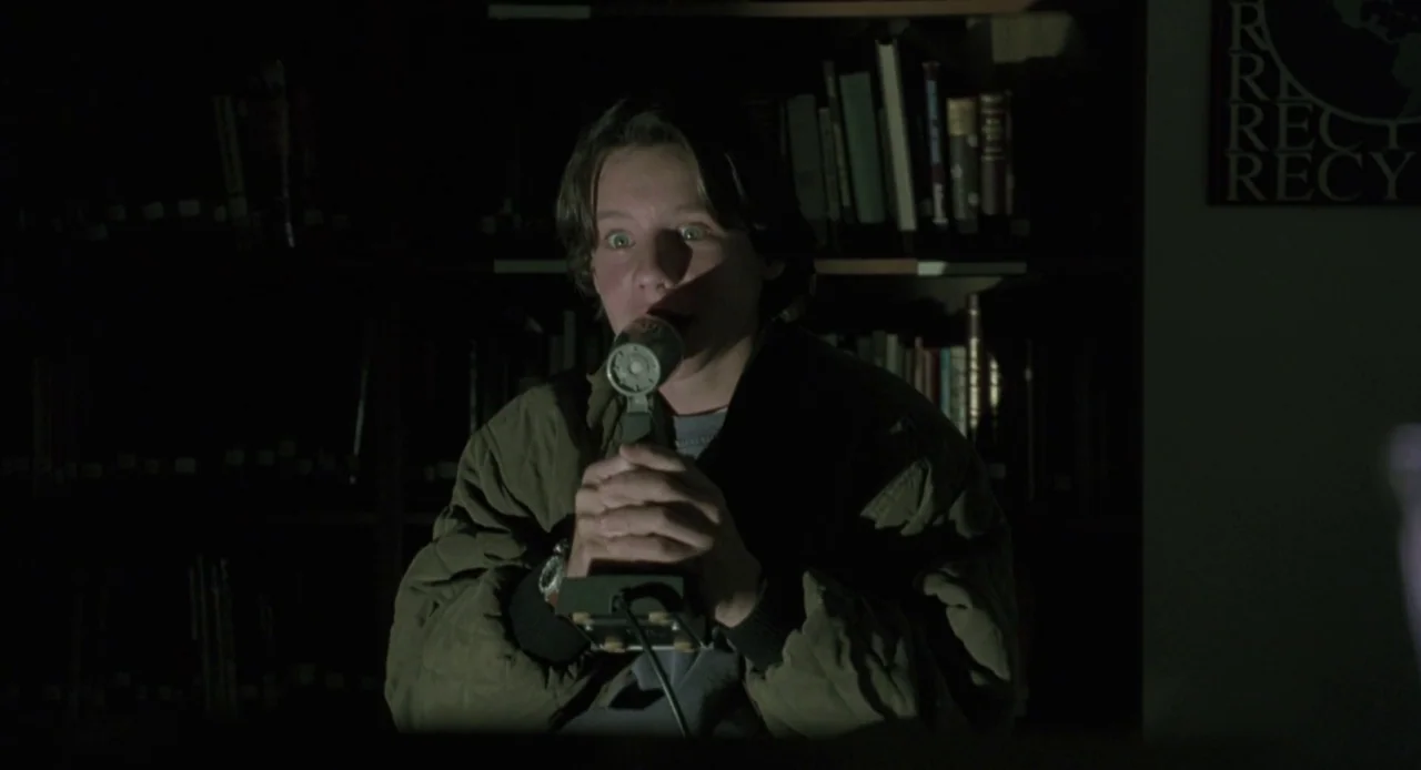 Hocus Pocus (1993) movie still: medium — A dimly lit space features a person positioned in front of dark wooden shelves. A young man sits in the…