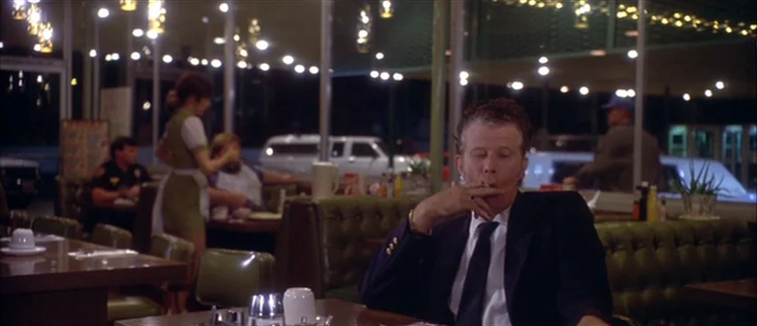 Short Cuts (1993) movie still: medium — A 1980s-style diner at night features green vinyl booth seating and glowing ceiling lights. A man in a suit…