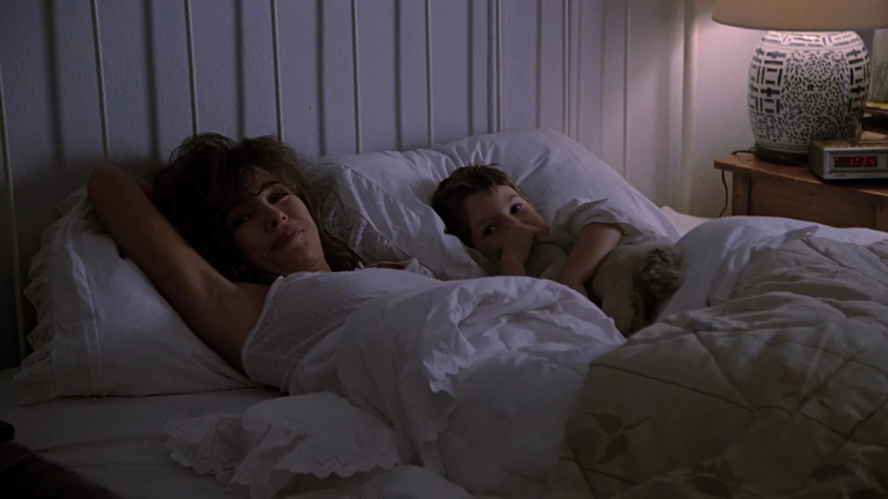 Fatal Attraction (1987) movie still: medium — A dark bedroom features a bed with white linens and a wooden headboard. A woman and child lie side by…