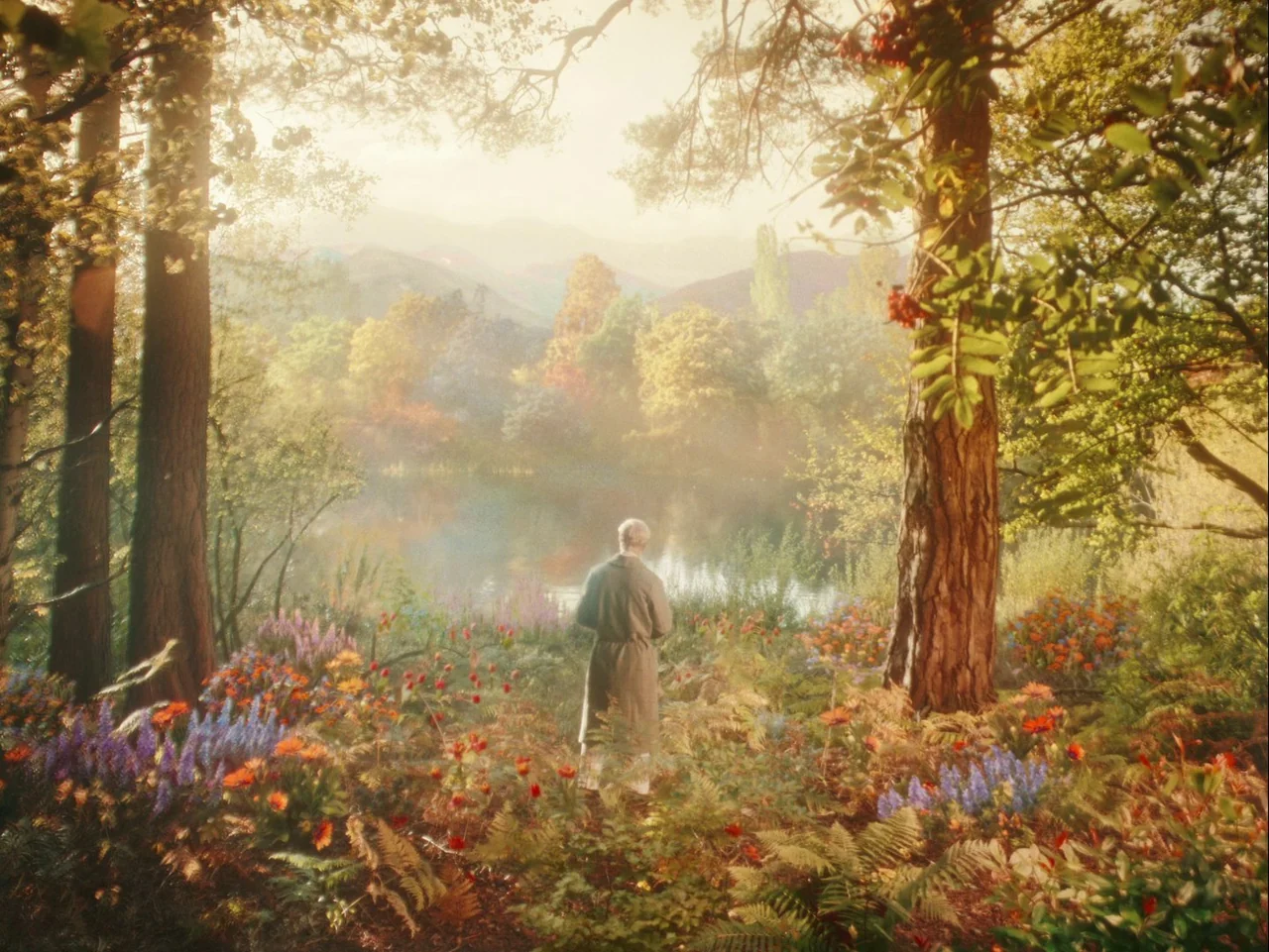 The Electrical Life of Louis Wain (2021) movie still: wide — A lush meadow filled with colorful wildflowers surrounds a calm lake under warm light.…