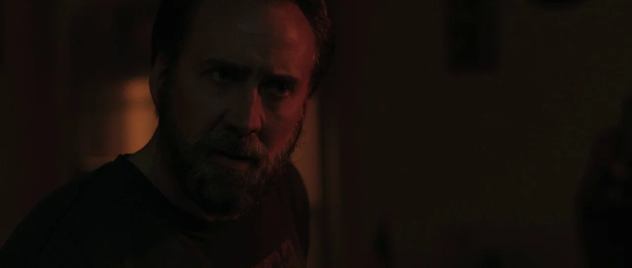Joe (2013) movie still: closeup — A dark indoor space is illuminated by a single warm light source. A middle-aged man stares intently off-camera…