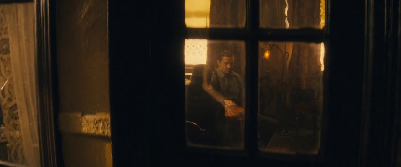 The Immigrant (2013) movie still: medium — A man and a woman sit together in a dimly lit room with amber curtains. The scene is viewed from the…
