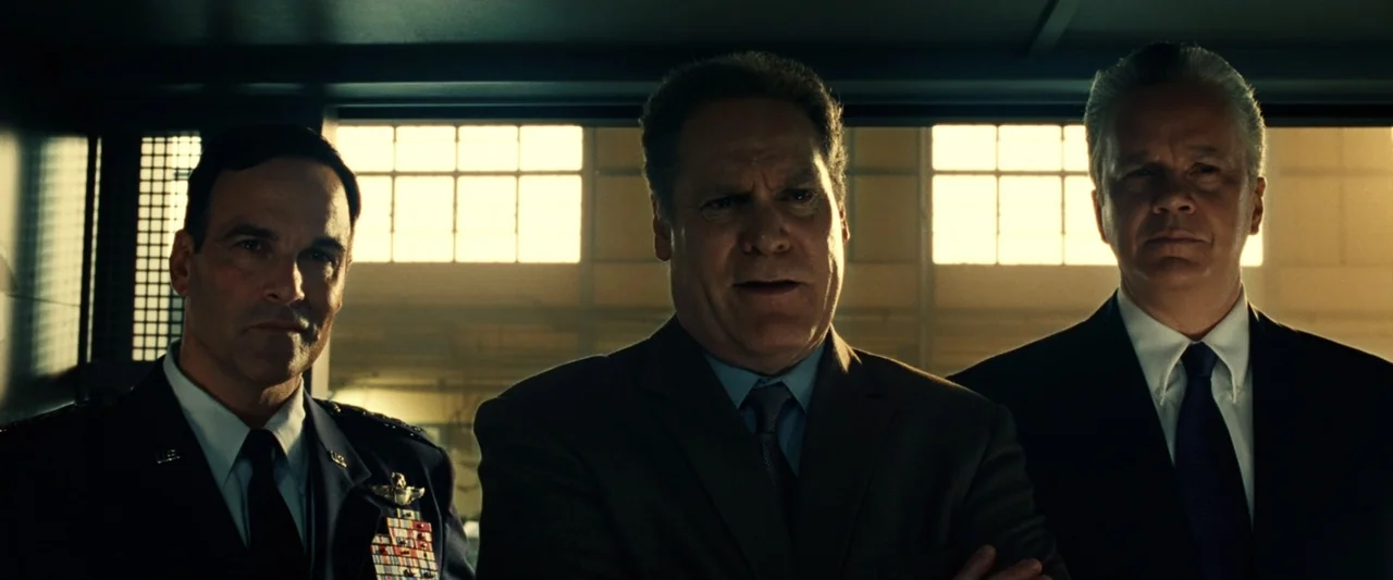 Green Lantern (2011) movie still: medium — A utilitarian room features large rectangular windows providing bright backlight to three men. Three men…