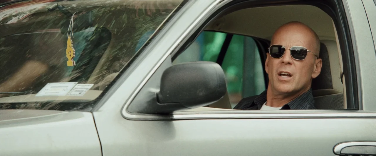Cop Out (2010) movie still: medium — The interior of a silver sedan with a pine tree-shaped air freshener hanging. A bald man wearing aviator…