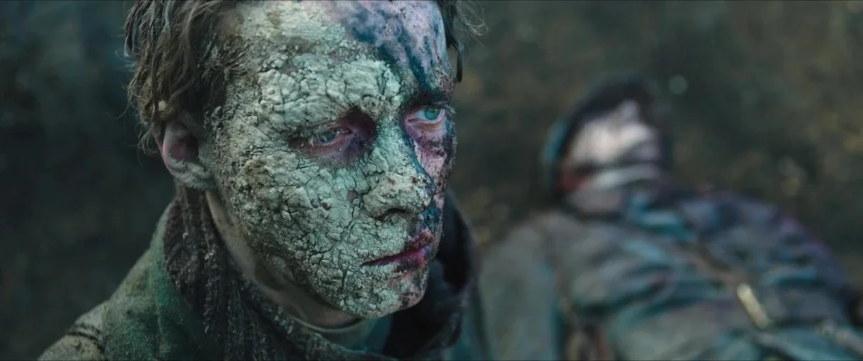 All Quiet on the Western Front (2022) movie still: closeup — A battlefield trench features muddy walls and two soldiers in damp, grimy uniforms. One…