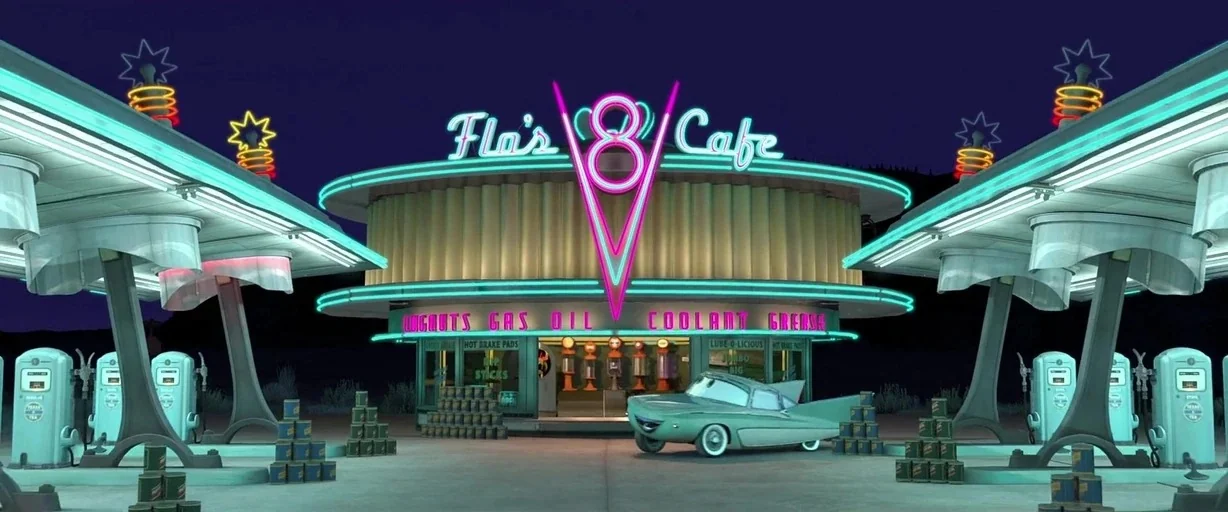 Cars (2006) movie still: wide — A stylized 1950s-inspired gas station at night with prominent glowing neon signage. A single light green car is…