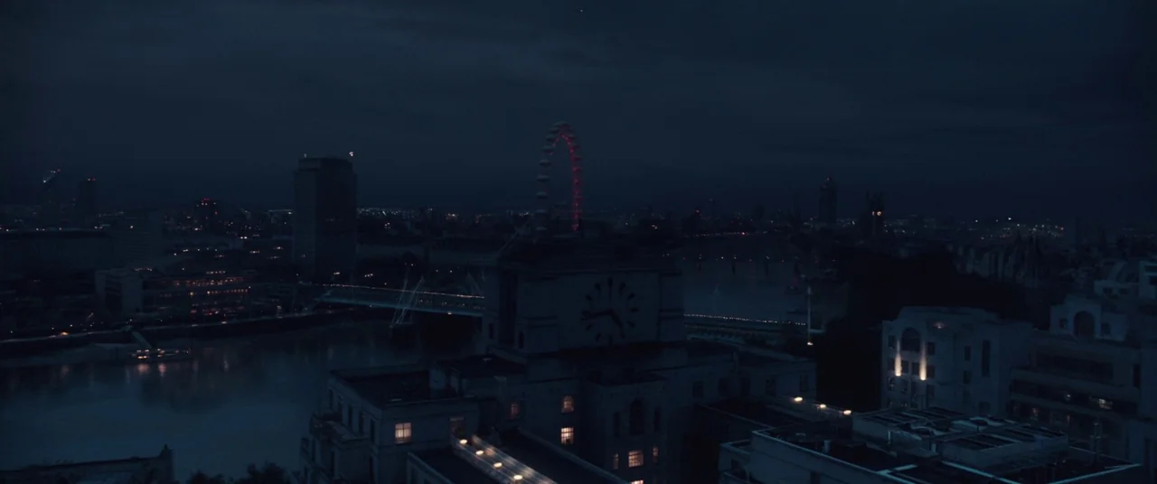 Assassin’s Creed (2016) movie still: establishing — A nighttime aerial view of London along the River Thames under a dark sky. The London Eye is…