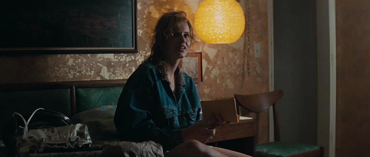 Thelma & Louise (1991) movie still: medium — A dimly lit room features patterned wallpaper and a prominent round paper pendant lamp. A woman sits on…