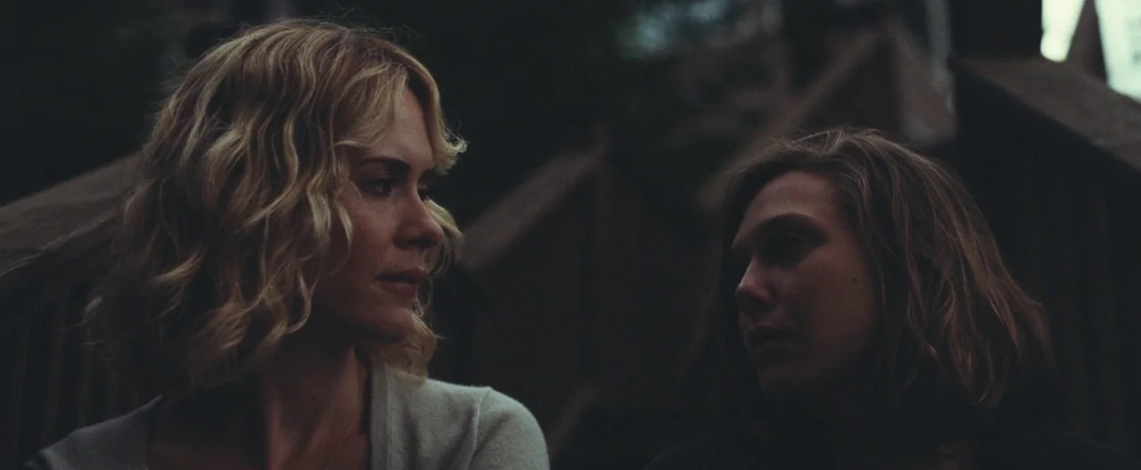 Martha Marcy May Marlene (2011) movie still: medium — Two women sit closely together on a set of wooden outdoor stairs at night. The pair look…