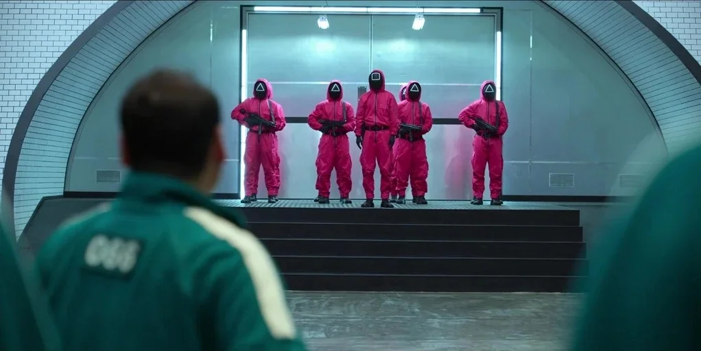 Making of: Squid Game (2021) movie still: medium — A clinical tiled bunker features a central raised metal platform with large double doors. Five…