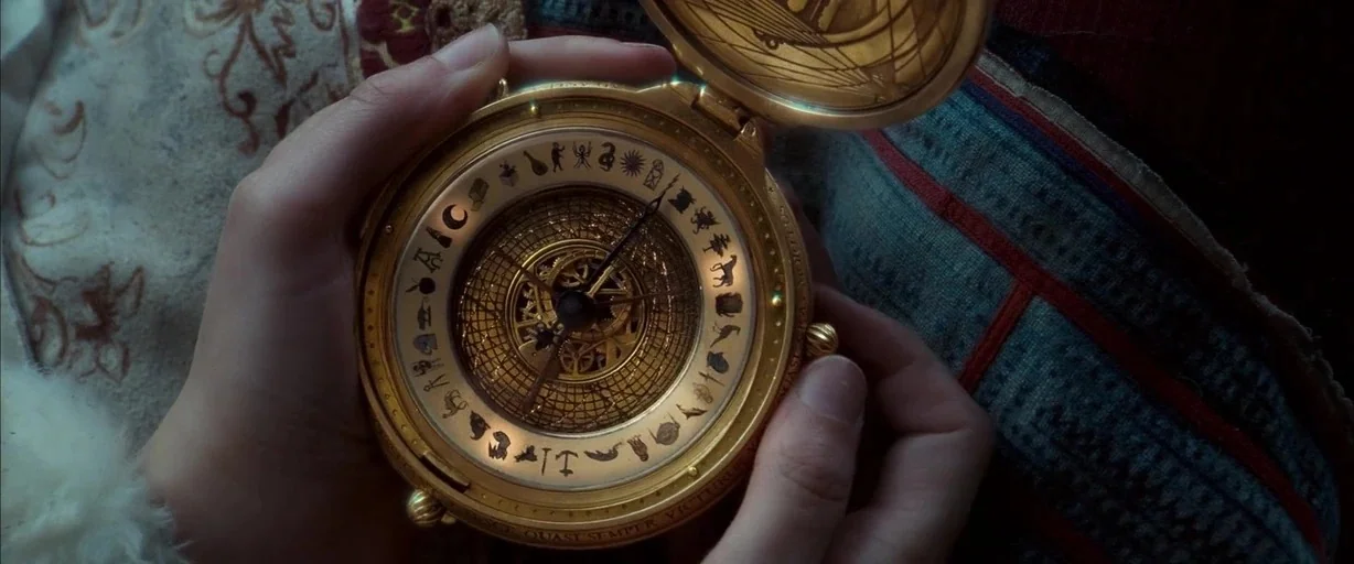 The Golden Compass (2007) movie still: closeup — A close view of a golden alethiometer held in a pair of hands. The device features intricate…