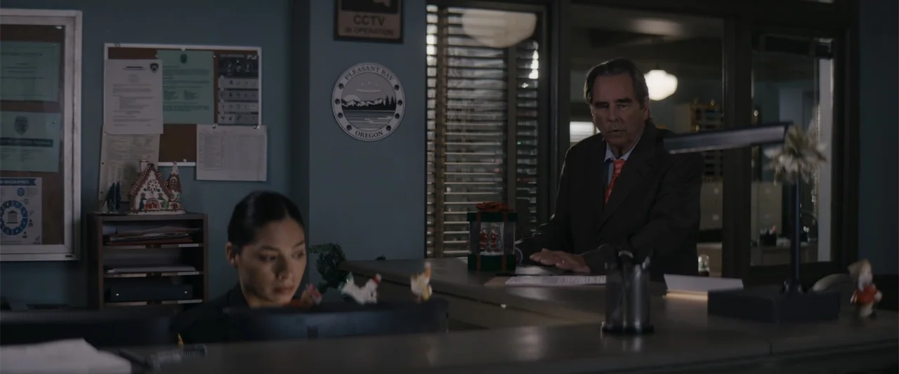 A Christmas Mystery (2022) movie still: medium — A police station reception area features a bulletin board, a wall emblem, and festive decorations.…