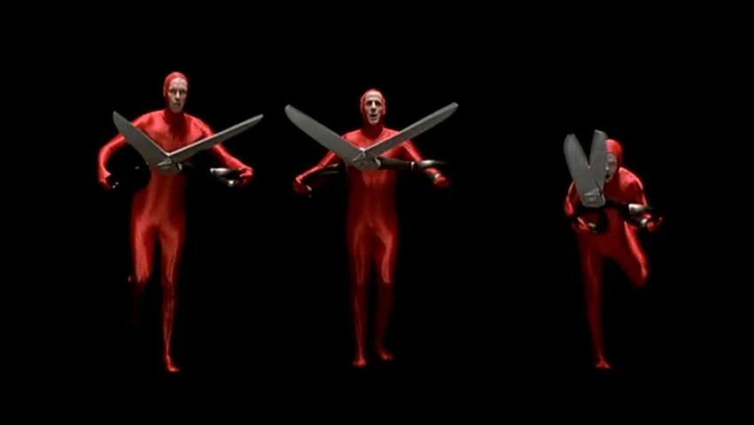 The Big Lebowski (1998) movie still: fullbody — Three individuals wearing identical red bodysuits stand against a completely black background. Each…