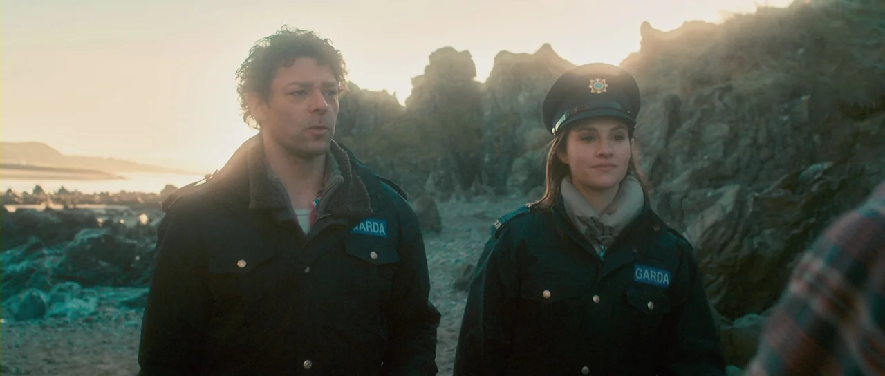 Grabbers (2012) movie still: medium — A rugged, rocky coastline at golden hour with distant shoreline visible in the background. Two police officers…