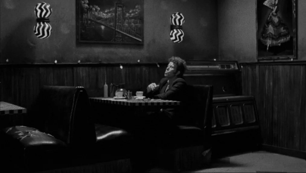Coffee and Cigarettes (2003) movie still: wide — A dark, wood-paneled diner booth features patterned wall sconces and framed artwork. A man sits…
