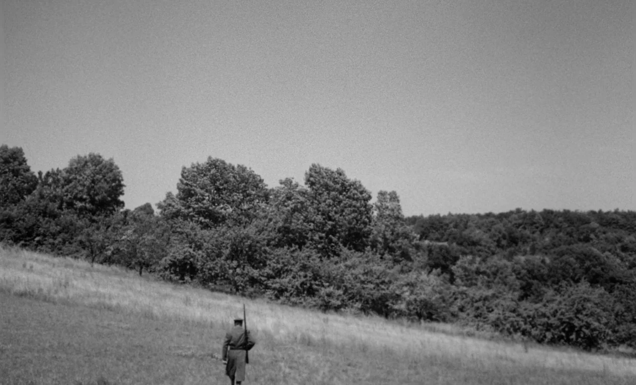 Goto, Island of Love (1969) movie still: wide — An open grassy slope meets a dense line of trees under an expansive sky. A soldier in a military…