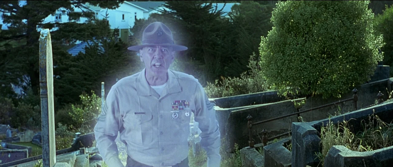 The Frighteners (1996) movie still: medium — A man in a military uniform stands in a cemetery with stone markers. He is shouting towards the camera…
