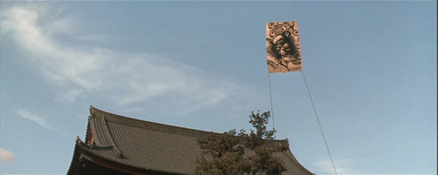 Kwaidan (1964) movie still: establishing — A traditional Japanese-style building features a dark tiled roof against a clear blue sky. A large…