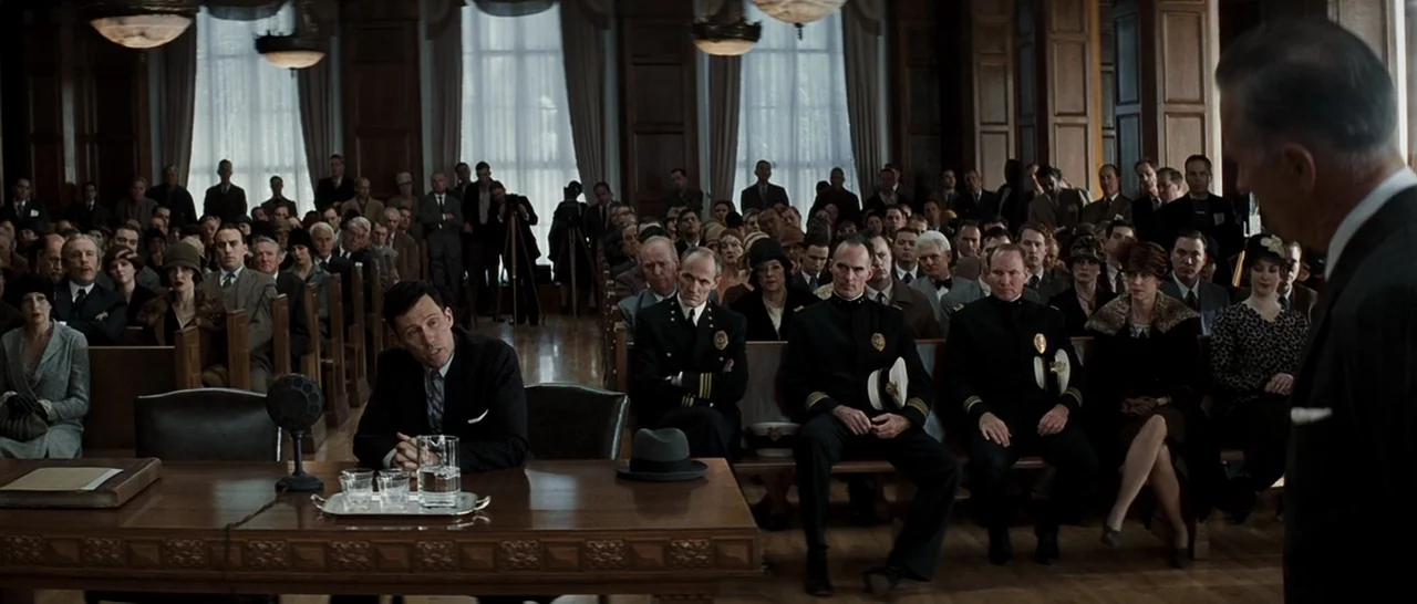 Changeling (2008) movie still: wide — A formal hearing room features wood-paneled walls and large windows with heavy curtains. A crowd of people…