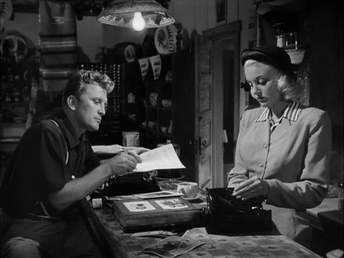 Ace In The Hole (1951) movie still: medium — An interior space with a wooden counter covered in documents and a small box. A man and a woman stand…