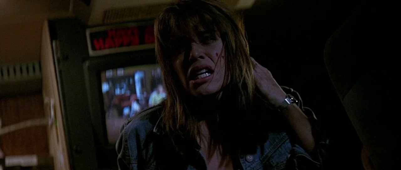 Scream (1996) movie still: medium — A dark vehicle interior with a glowing digital screen displaying text in the background. A woman in a denim…